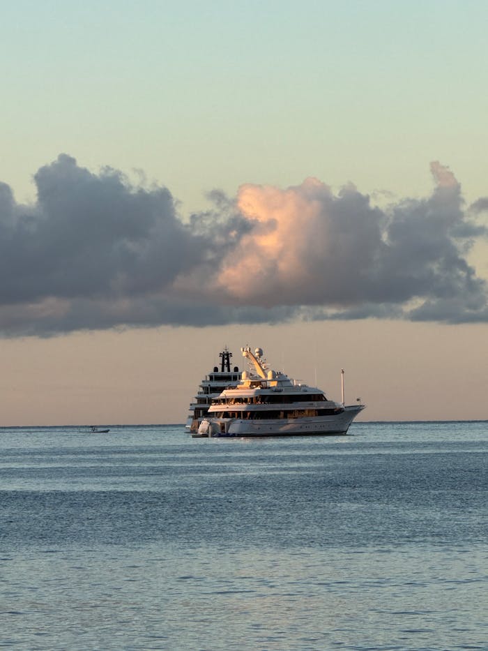 Serene sunset view of a yacht cruising on tranquil sea, under beautifully clouded sky.