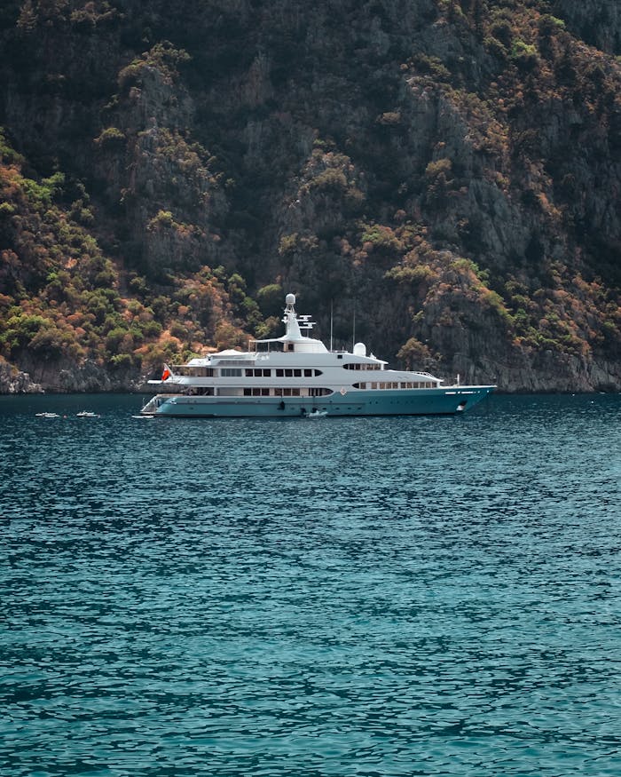 A luxury yacht sailing through clear blue waters against a rocky coastal backdrop.