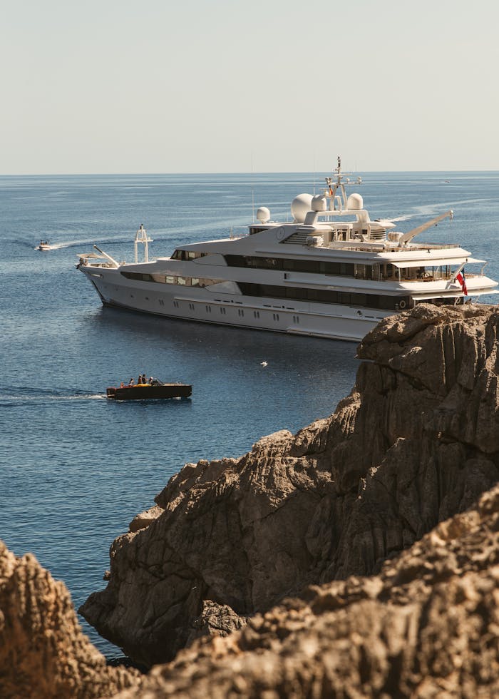 A luxury yacht cruising near rocky cliffs on a sunny day in Spain, showcasing adventure and travel.